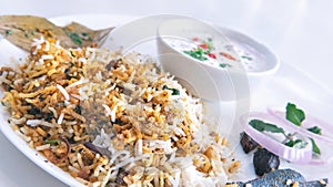 Tilt shot of delicious Indian Hyderabadi biryani with curd and salad in a white background