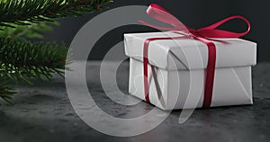Tilt shot of spruce twig with white gift box with red ribbon on terrazzo countertop