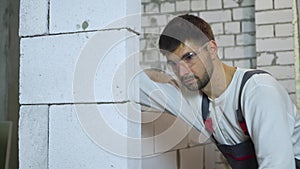 Tilt shot of young builder in work wear grinding block wall with abrasive tool