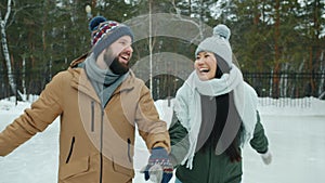 Tilt-up of happy couple Caucasian man and Asian woman ice-skating laughing outdoors in park