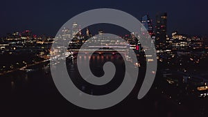 Tilt up reveal of city centre at night. Illuminated bridges over river and buildings on waterfront. Group of skyscrapers