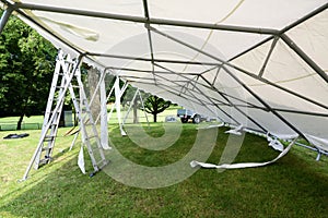 Tilted  event tent during set up and ladders on the lawn in a park for a summer party or wedding