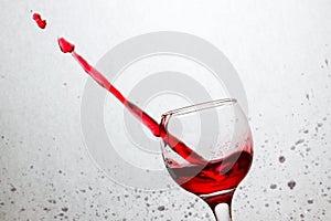 Tilted glass of red wine pierced a stream of alcoholic beverage