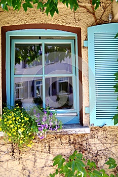 Tilted window with turquoise frame and shutter with flower decorations