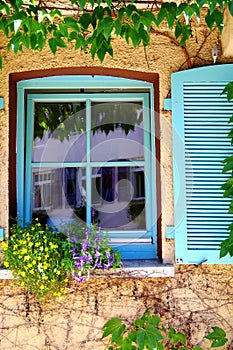 Tilted window with turquoise frame and shutter with flowers