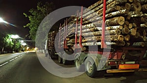 Timber truck loaded with logs. A heavy-duty vehicle with a forest stands on the side of the road at night. Harvesting trees in