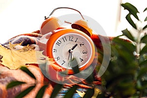 Time for beautiful autumn days: an orange alarm clock is wrapped in a warm shawl, rowan branches nearby, bokeh, close-up