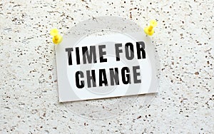 TIME FOR CHANGE is written on a card attached to a white textured wall with a button. Office reminder.