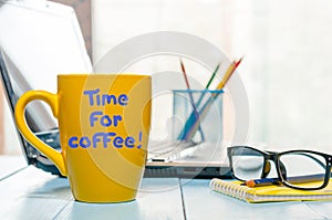 Time for coffee written on yellow cup at business office workplace background. Fun calligraphy typography greeting and