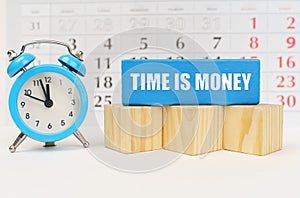 Against the background of the calendar is an alarm clock, cubes and a blue block with the inscription - Time Is Money