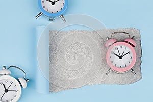Time concept. alarm clock through hole in blue paper background