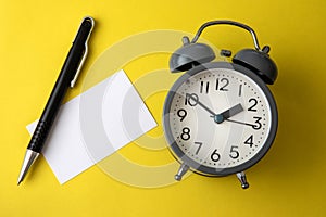 Time concept with blank white paper note copy space to add wording or message , a alarm clock with black pen decoration on yellow