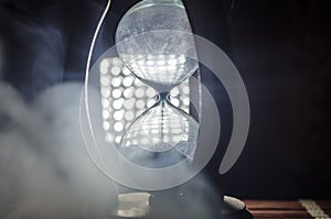 Time concept. Silhouette of Hourglass clock and smoke on dark background with hot yellow orange red blue cold back lighting, or sy