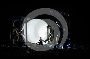 Time concept. Silhouette of a man standing between hourglasses with smoke and lights on a dark background.