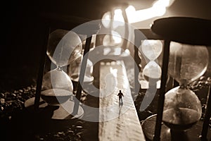 Time concept. Silhouette of a man standing between hourglasses with smoke and lights on a dark background. Surreal decorated