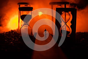 Time concept. Silhouette of a man standing between hourglasses with smoke and lights on a dark background. Surreal decorated