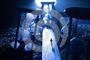 Time concept. Silhouette of a man standing between hourglasses with smoke and lights on a dark background. Surreal decorated