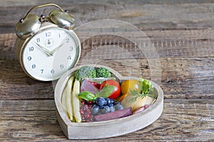 Time on diet concept with alarm clock and healthy food in heart