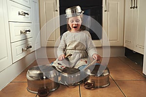 Time for a drumroll. a little girl playing drums on a set of pots in the kitchen.