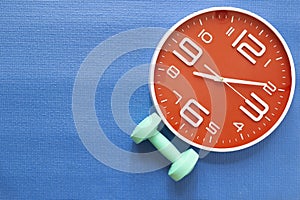 Time for exercising clock and dumbbell with blue yoga mat background