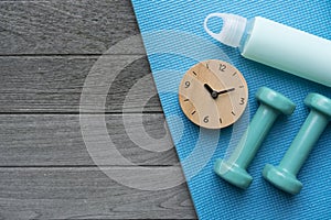 Time for exercising clock and dumbbell with yoga mat background