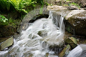 Time exposure photo shot with a small waterfall over rocks in a stream and milky blurred water