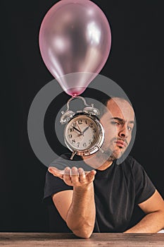 Time flies concept - picture of a man looking at the camera while placing his hand underneath an old metal clock