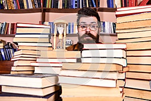 Time flow concept. Teacher or student with beard studying in library. Man, scientist in glasses looks at hourglass. Man