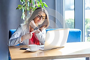 Time is gone. Portrait of serious young woman in glasses sitting, looking at laptop screen on video call and pointing at her smart