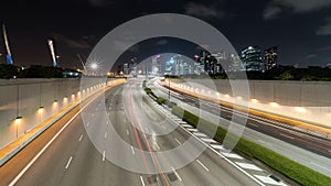 Time-lapse of car traffic transport on multiple lanes highway, financial district buildings, crane construction at night