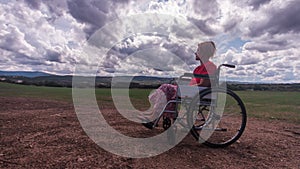 Time lapse of a disabled girl sitting in a wheelchair in the middle of a green field in the countryside with a sky full of