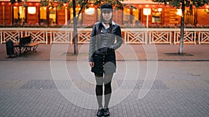Time-lapse portrait of serious Asian woman in stylish clothes standing in the street in the evening and looking at