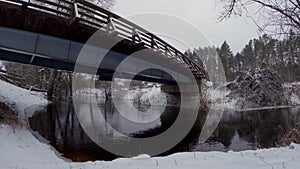 Time lapse of river flowing under the bridge on a cloudy winter day. Water stream next to the village and the woods