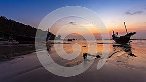 Time lapse of small fishing boat lay on beach and reflection of water and yellow, orange sunset color on beach in sunset time of T