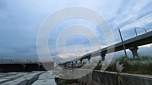 Time lapse of sunset metrorail flyover  under running vechicles and grass flowers