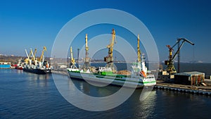 Time-lapse video of cargo ship docking at busy port, cranes loading containers during sunrise. Maritime transport