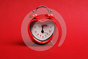 Time for love. Red heart shaped alarm clock on red background