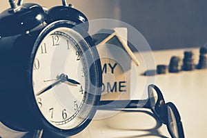 Alarm clock on working table with eyeglass and home replica