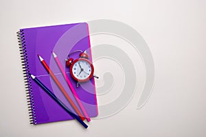 Time management concept. Red vintage alarm clock, pencils and purple notepad