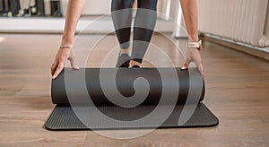 Time for meditation, fitness session, well-being concept. Girl wearing black sporty pants rolling fitness mat before