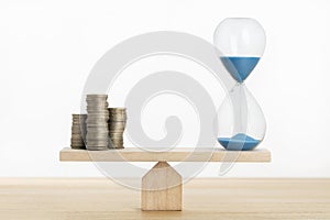 Time and money balance concept. Sand clock and stacked coins on Seesaw