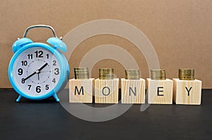 Time is money concept with alarm clock, coins and the word written on wooden cubes. A valuable resource for making money in busine