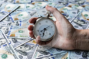 Time is money concept. A stopwatch in a hand on one hundred dollars notes as a background