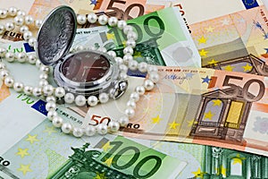 Time is money concept, traditional pocket watch with pearls on Euro banknotes