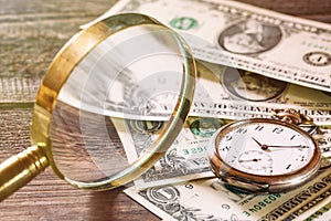 Time is money finance concept with old vintage clocks, dollar bills and magnifying glass on wooden table