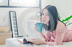 Time for myself. Comfort and relaxation. Pretty young asian woman drinking tea or coffee and reading book while sleeping