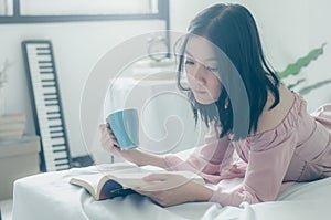 Time for myself. Comfort and relaxation. Pretty young asian woman drinking tea or coffee and reading book while sleeping