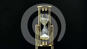 Time passing while sand falls through hourglass. Black background