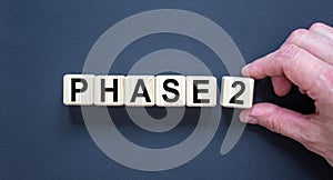 Time for Phase 2. Hand holds a cube with number `2`. Word `Phase 2`. Beautiful black background. Business concept. Copy space