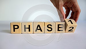 Time for Phase 2. Hand is turning a cube and changes the word `Phase 1` to `Phase 2`. Beautiful white background. Business con